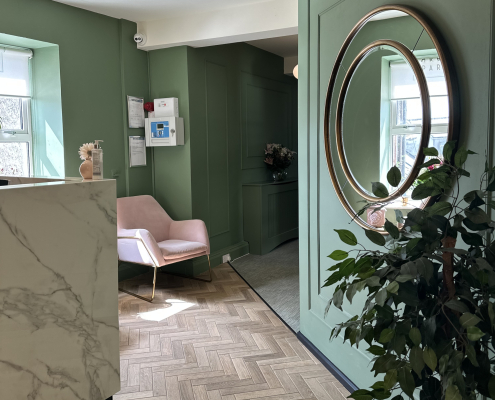 Office reception with green walls, pink armchair and white marble reception desk