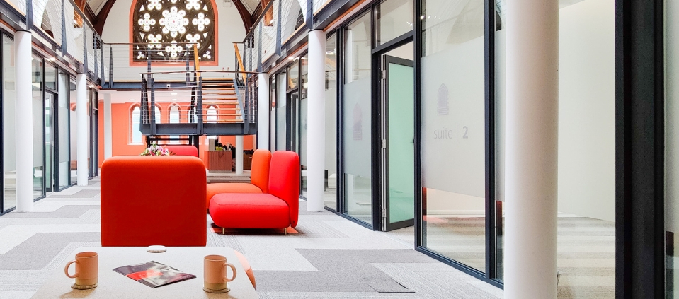 Office space in modernised church. Red seating and grey carpet with white architecture