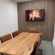 Office boardroom with wood pannelling feature on back wall, a wooden oak table with brown chairs and a picture of a fire on a tv mounted on the wall.